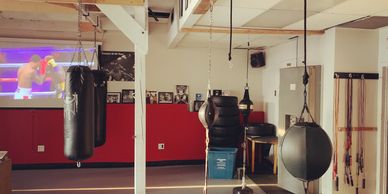 Boxing gym with punching bags and TV screen showing a match.