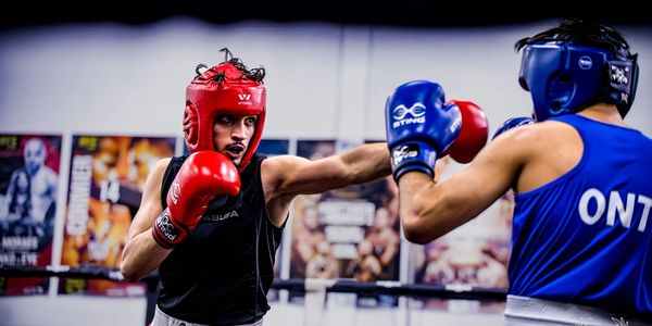 Two boxers sparring in a gym wearing red and blue headgear.