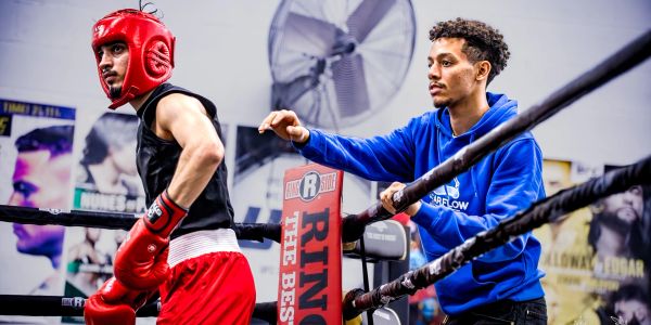 Boxer in red gear receiving coaching in ring.