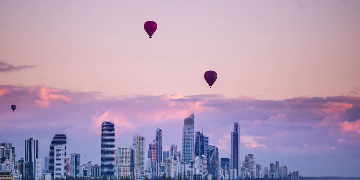 Purple hot air balloons above a city skyline at sunset.