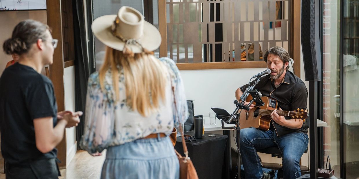 Man playing guitar and singing indoors while two people watch.