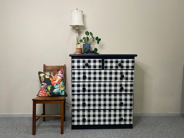 Black and white checkered dresser next to wooden chair with floral pillow.