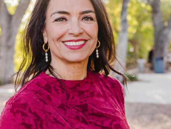 Smiling woman in a textured red dress with pearl earrings outdoors.