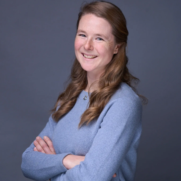 Smiling woman in blue sweater crossing her arms.