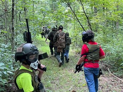 Group of people in tactical gear walking through a forest trail.