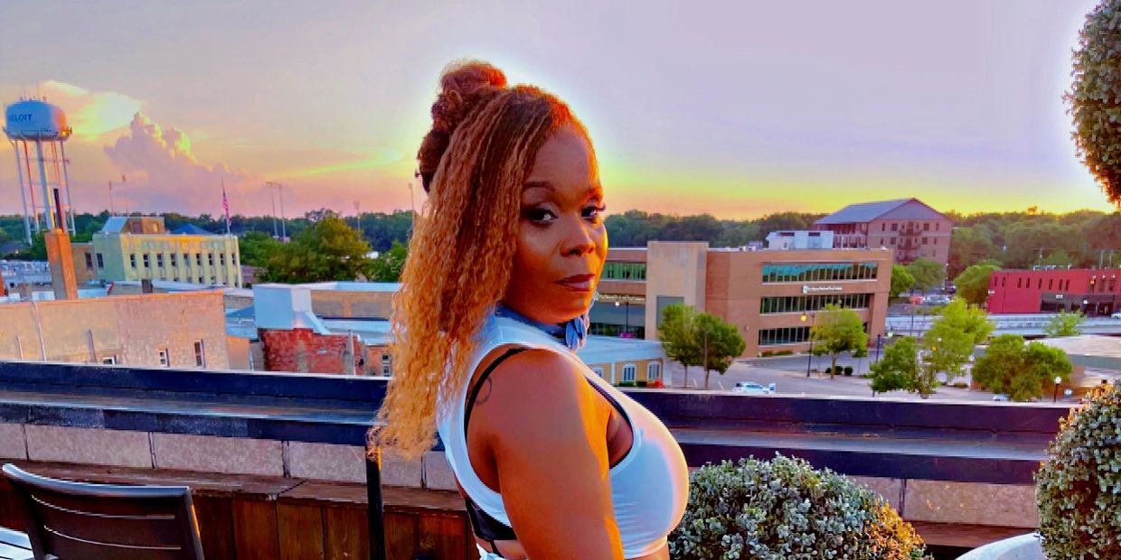 Woman in white dress holding a blue clutch on a rooftop at sunset.