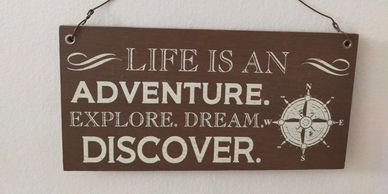 Wooden sign with inspirational life adventure quote and compass.