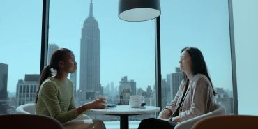 Two women chatting in a cafe with cityscape.