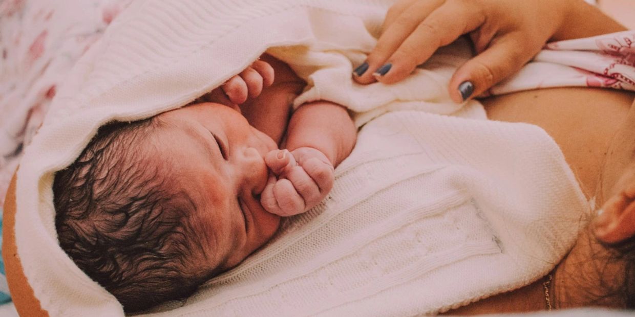 Newborn baby wrapped in blanket in mother's arms.