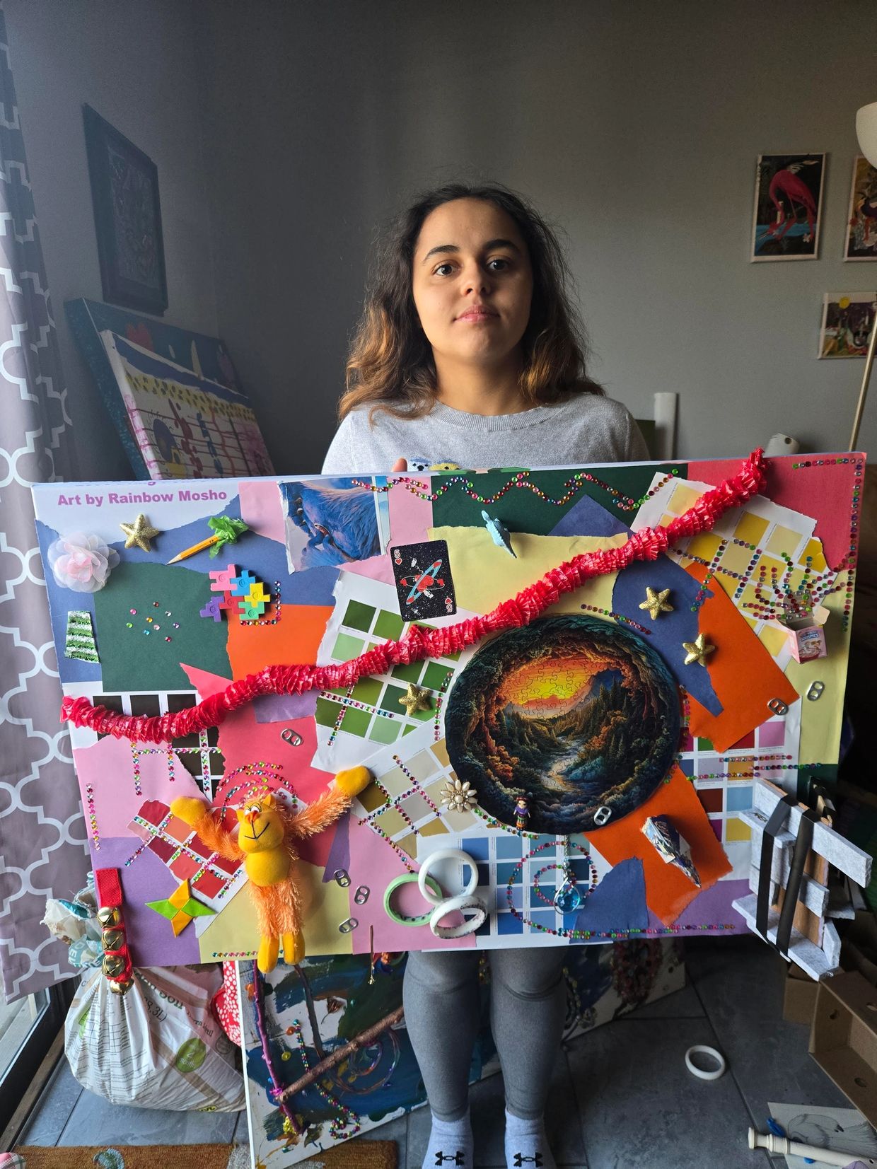 Young woman holding a colorful, mixed-media art board with various decorations.