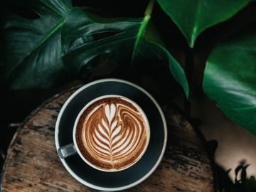two coffee lattes with leaves on wood surface