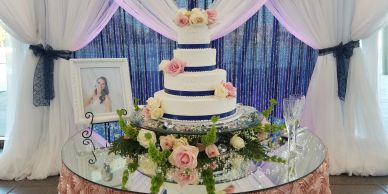 Elegant three-tier wedding cake decorated with pink roses and greenery on a glass table.