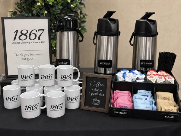 Coffee service setup with mugs, dispensers, and sweeteners at 1867 Artistic Catering Solutions.
