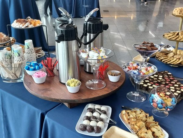 Coffee and dessert buffet with treats and condiments on a blue tablecloth.