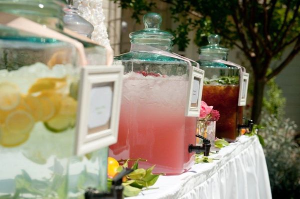 Three large glass dispensers with different refreshing beverages on a white table.