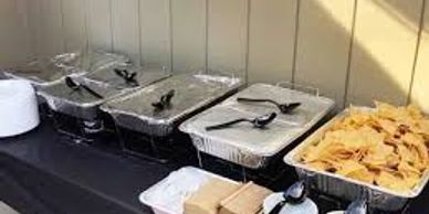 Catering trays with food and chips set on a black tablecloth.
