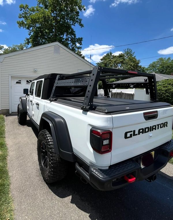 White Jeep Gladiator truck with black rack and off-road tires parked in driveway.