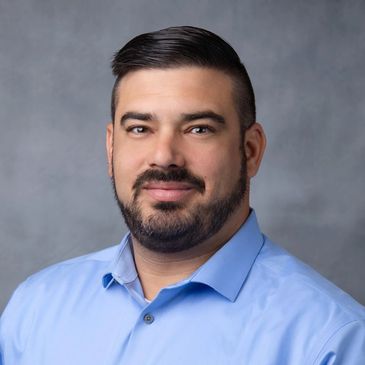 Portrait of a man with a beard and light blue shirt.