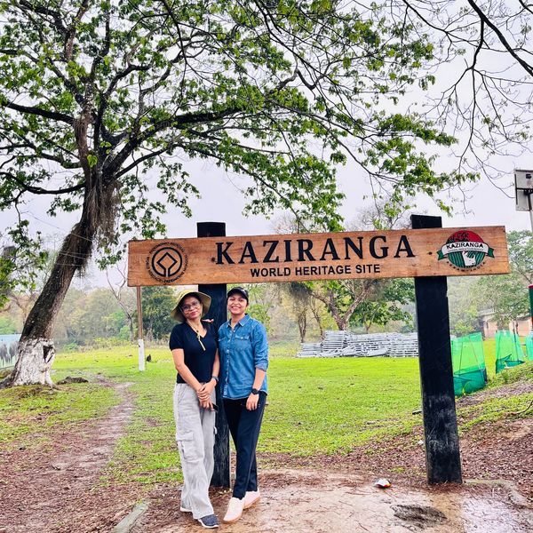 Two people posing under the Kaziranga World Heritage Site sign amidst greenery.