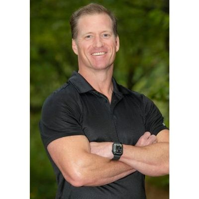 Smiling man in black polo shirt with arms crossed outdoors.