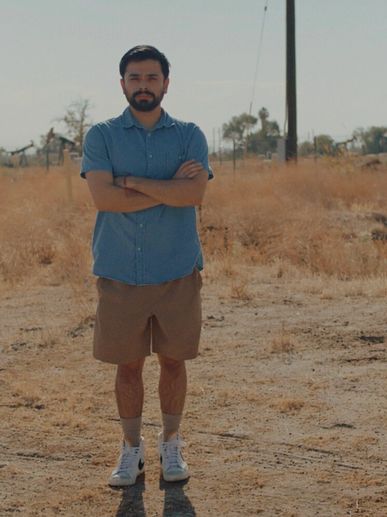 Man standing with arms crossed in dry field with oil pumps.