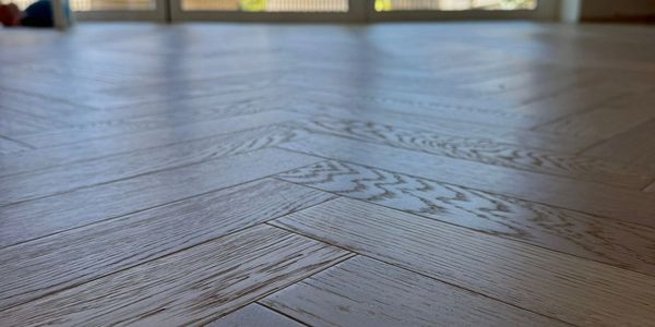 Close-up of wooden floor with herringbone pattern under natural light.