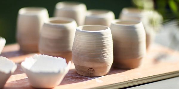 Handcrafted ceramic cups and bowls on a wooden board.