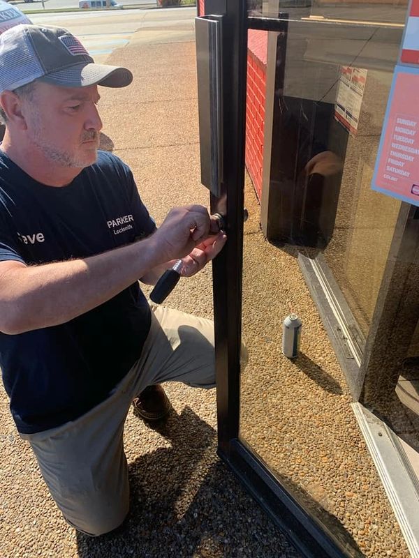 A locksmith kneeling and fixing a lock on a glass door outside.