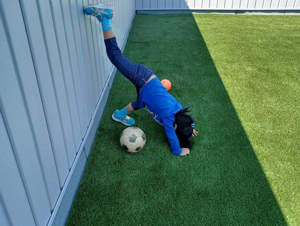 Child in blue doing a handstand near a wall with a soccer ball.