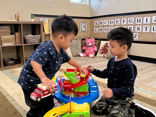 Two boys playing with toy cars on a colorful track in a classroom.