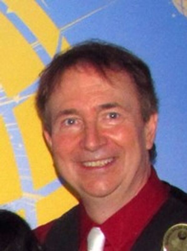 Smiling man in red shirt and white tie against a colorful background.