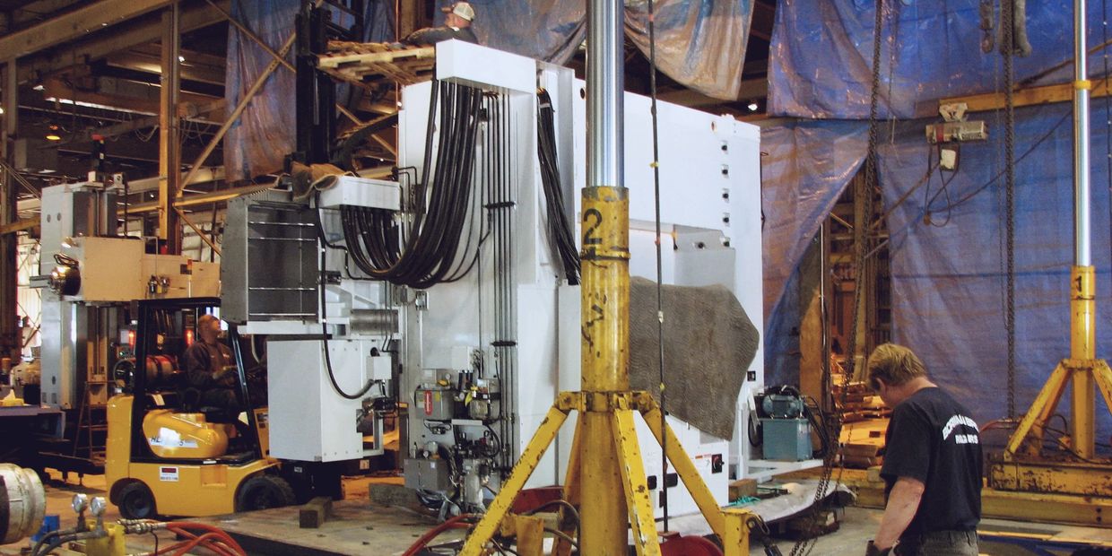 Workers operate heavy machinery and forklift in an industrial warehouse.