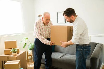 Younger man helping to lift a box with an elderly man.