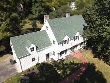 White two-story house with green roof and a curved brick pathway.