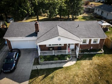A single-story brick house with a porch and two cars parked outside.