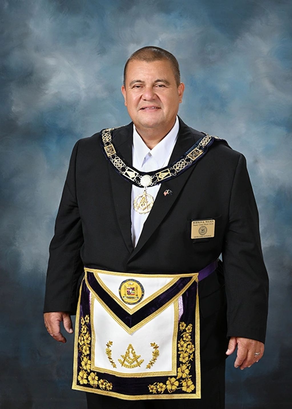 Man in Masonic regalia with apron and collar against a blue-gray backdrop.