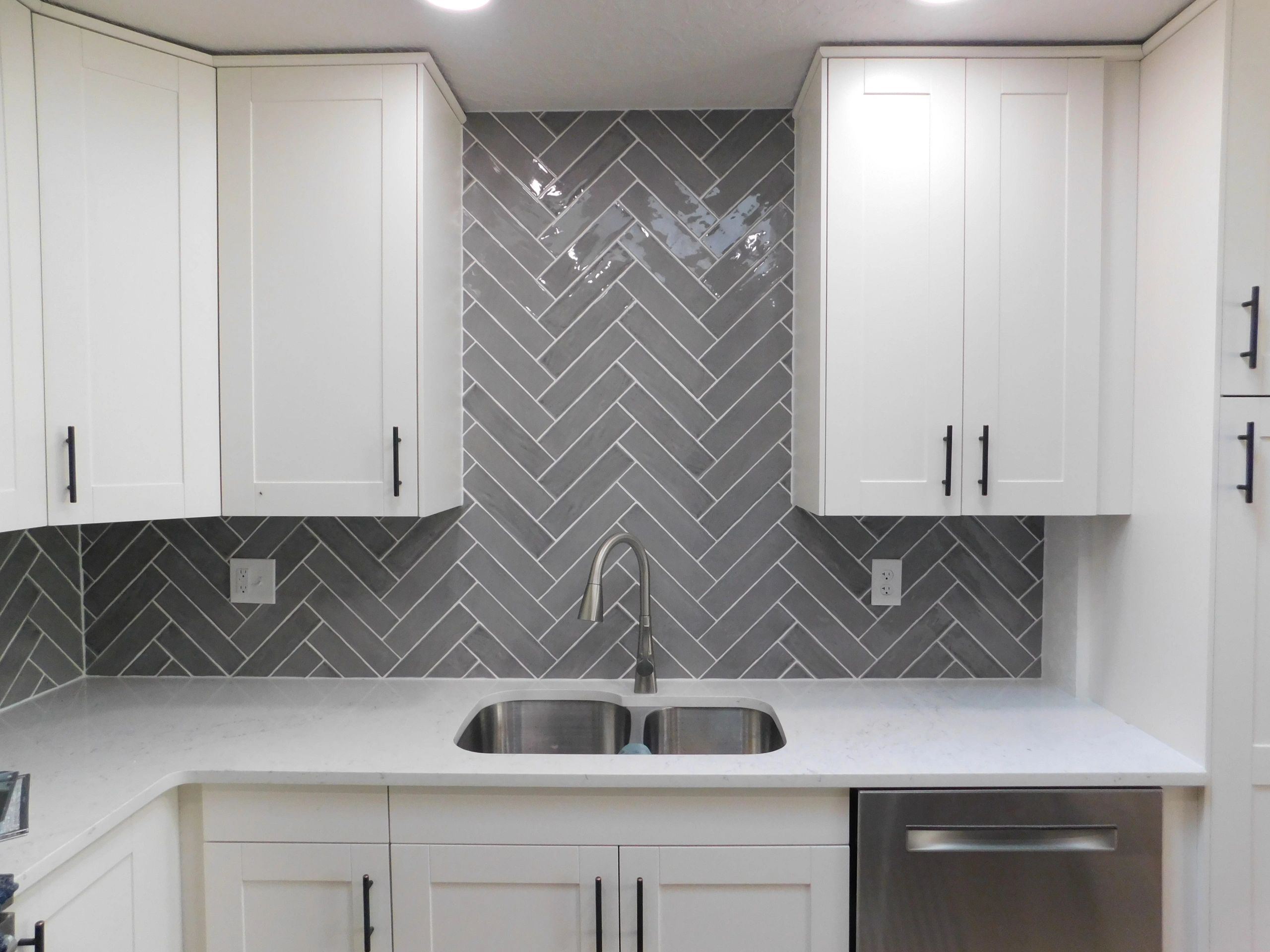 White kitchen cabinets with gray herringbone backsplash. 