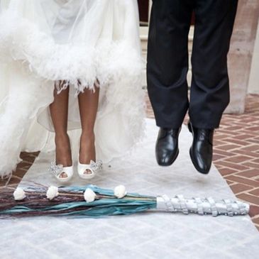 Bride and groom jumping over a floral arrangement at their wedding.