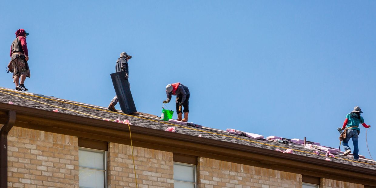 Construction workers repairing a roof under clear blue sky.