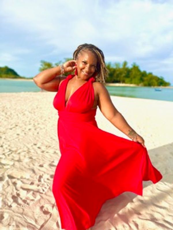 Woman in a flowing red dress poses on a sunny beach.