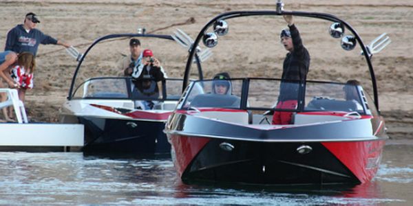 Two motorboats with people near a sandy shore, one person waving.