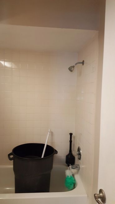Empty bathtub with cleaning tools and a large black bucket.