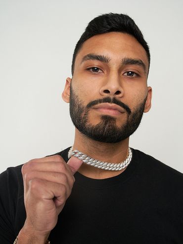 "Close-up portrait of man holding iced-out Cuban link chain, wearing black shirt and gold bracelet"