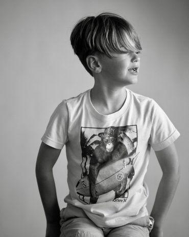 Black and white portrait of young boy in graphic tee looking off-camera in natural light