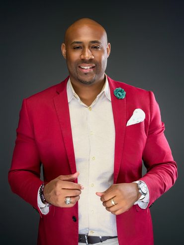 Confident man in red blazer posing for professional studio headshot against dark background