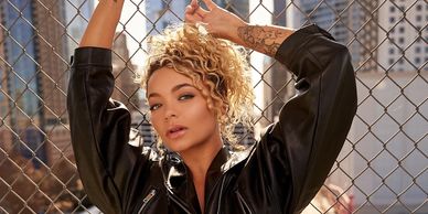 Editorial-style portrait of a tattooed woman posing confidently in front of a chain-link fence downtown.
