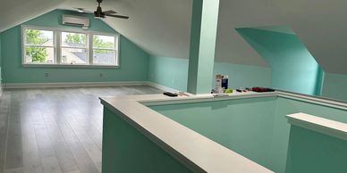Bright attic room with teal walls and light wood flooring under a sloped ceiling.