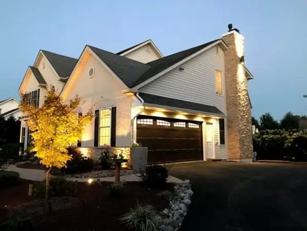 Modern suburban house illuminated at dusk with a glowing tree and stone chimney.