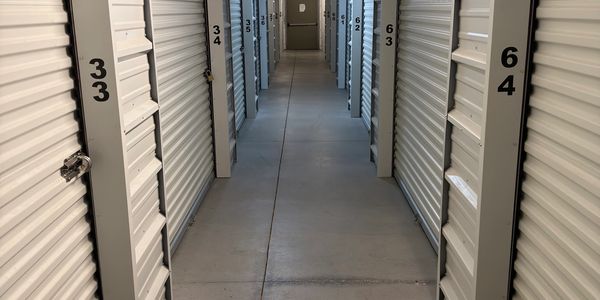 Corridor of numbered storage units with roll-up doors.
