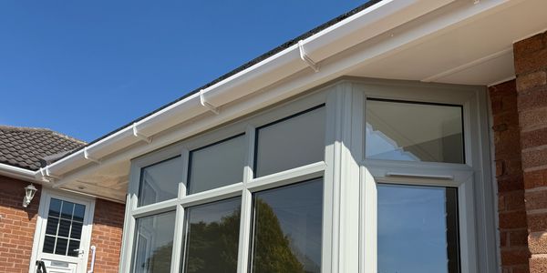 A modern conservatory with large glass windows attached to a brick house under a clear blue sky.